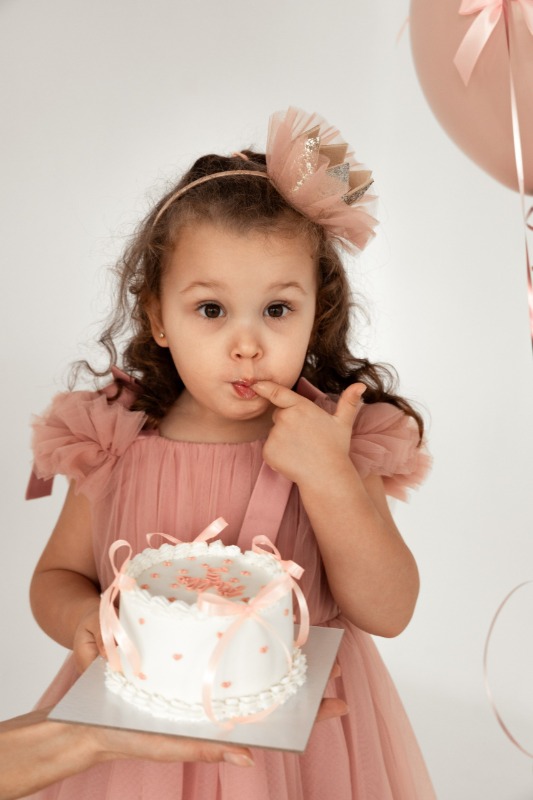 Маленькая девочка в розовом платье с бантом держит праздничный торт