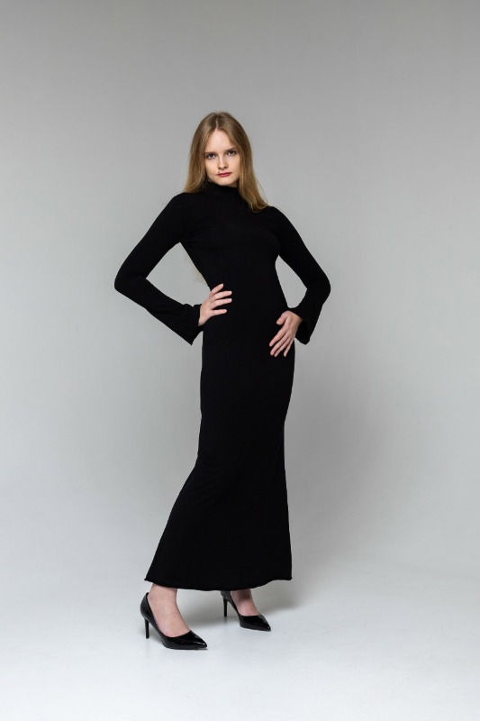 Девушка в длинном черном платье позирует на сером фоне