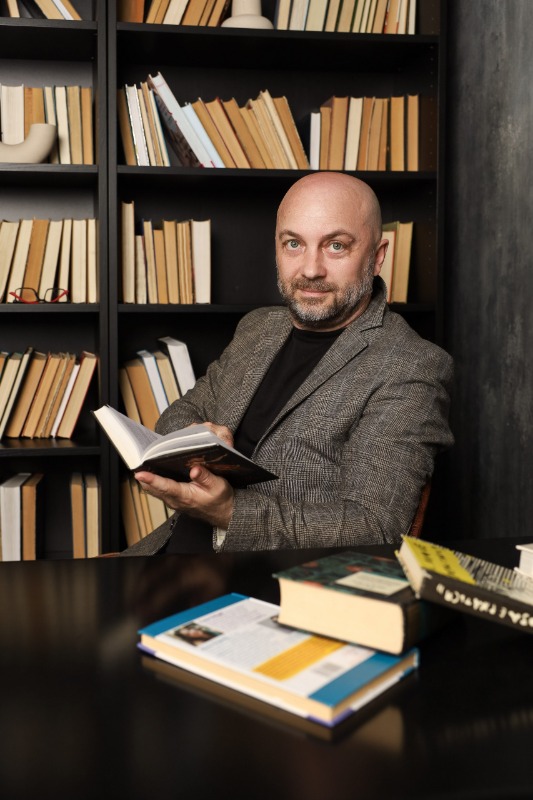 Мужчина в твидовом пиджаке с книгой за столом