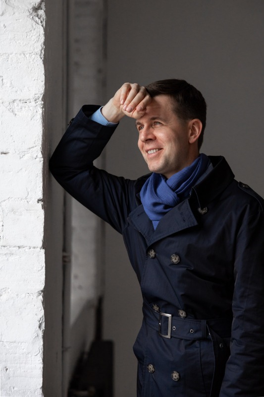 Мужчина в синем пальто у белой стены