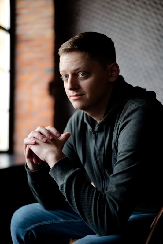 Молодой человек в темной толстовке у окна