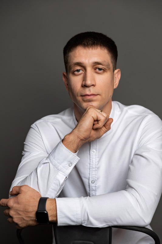 Мужчина в белой рубашке сидит на стуле на сером фоне