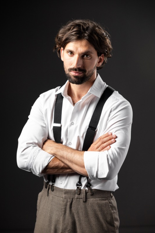 Мужчина в белой рубашке с подтяжками на темном фоне