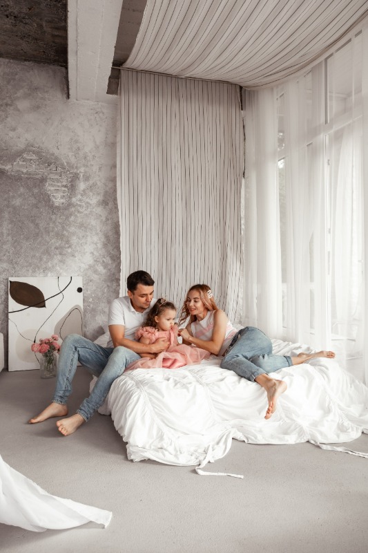 Семья из трех человек сидит на кровати в светлой спальне